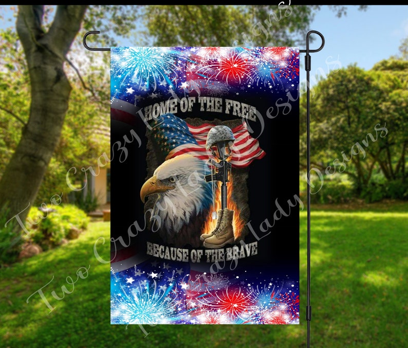 May include: A patriotic garden flag featuring an American flag, an eagle, and a soldier's memorial with a helmet, boots, and rifle. The flag has the text "HOME OF THE FREE BECAUSE OF THE BRAVE" with red, white, and blue fireworks.