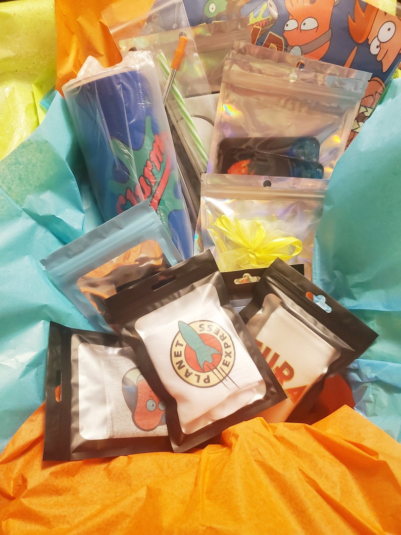 May include: A gift basket filled with various items, including a blue and green insulated tumbler with the word "SLURM" on it, a white t-shirt with a rocket ship and the words "PLANET EXPRESS" on it, and a white t-shirt with the word "RIP" on it. The basket is lined with blue and orange tissue paper.