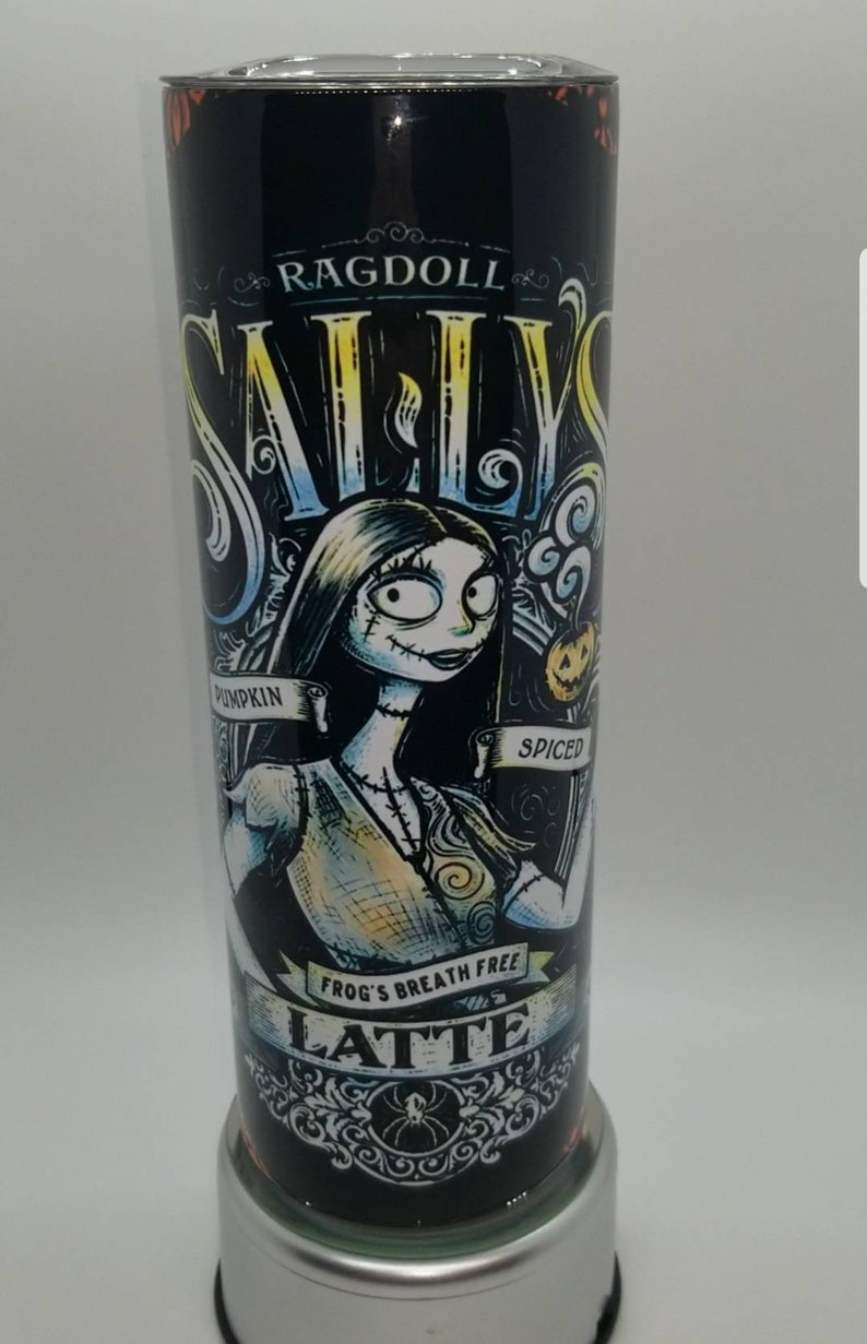 May include: A black and white tumbler with a graphic of Sally from The Nightmare Before Christmas. The text on the tumbler reads "Ragdoll Sally's Pumpkin Spiced Frog's Breath Free Latte".