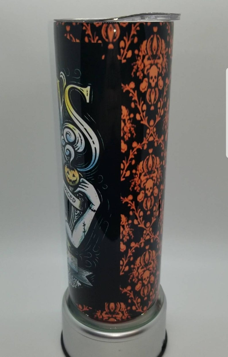 May include: A black and orange stainless steel tumbler with a Halloween-themed design. The design features a skull and crossbones, a pumpkin, and the text "Spiced".
