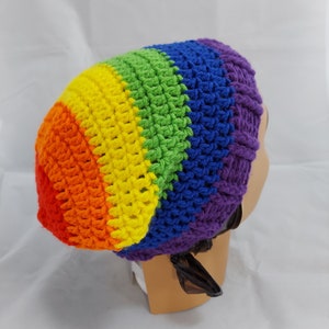 Op de afbeelding: Een regenbooggebreide beanie met een kleurpatroon in paars, blauw, groen, geel, oranje en rood. De beanie zit op een mannequinhoofd.