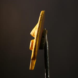 Op de afbeelding: Een gele keramische wandhaak met een uniek, abstract ontwerp. De haak is gemonteerd op een zwarte metalen staaf.