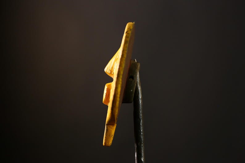 Op de afbeelding: Een gele keramische wandhaak met een uniek, abstract ontwerp. De haak is gemonteerd op een zwarte metalen staaf.