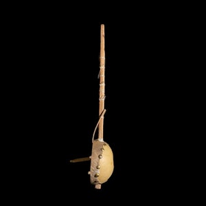 May include: A wooden musical instrument with a round, light brown gourd-like body and a long, thin wooden neck. The gourd is decorated with metal studs and a piece of leather.