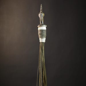 May include: A long, thin, brown whisk broom with a wooden handle and a white and brown decorative top.