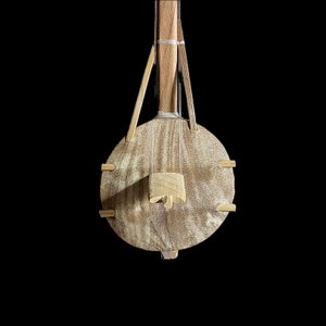 May include: A wooden musical instrument with a round body and a long neck. The instrument is made of light brown wood and has a simple design.