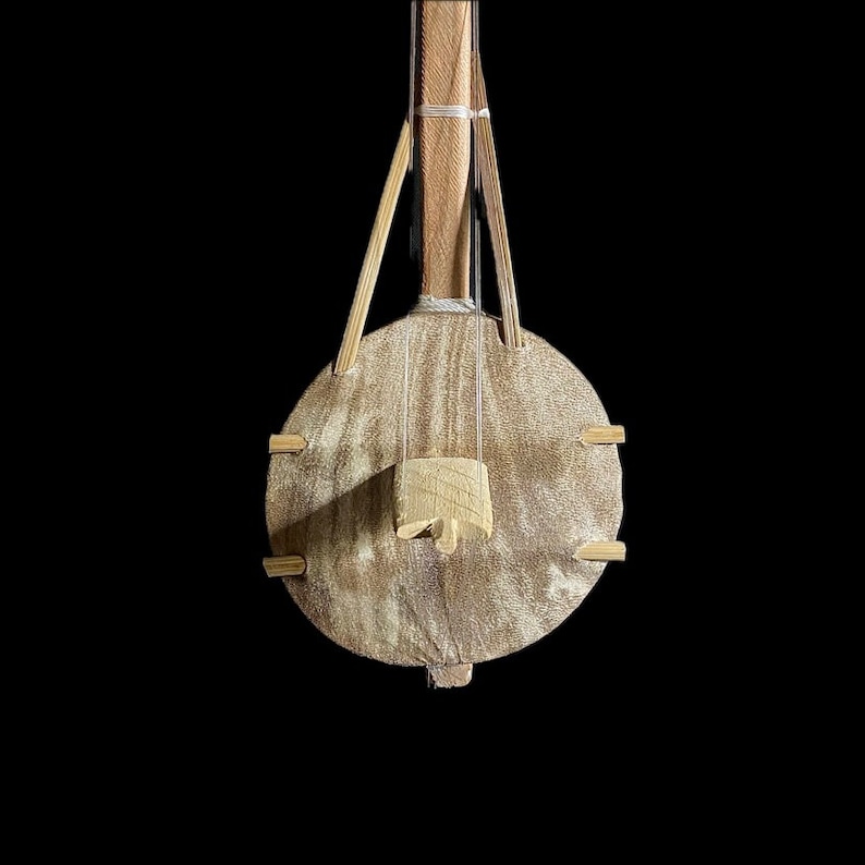 May include: A wooden musical instrument with a round body and a long neck. The instrument is made of light brown wood and has a simple design.