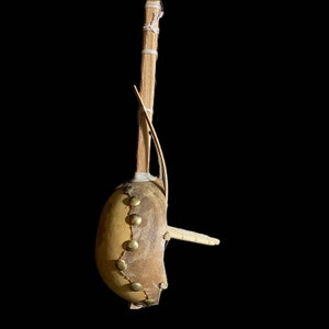 May include: A traditional musical instrument made from a gourd, wood, and string. The gourd is covered in leather and has brass tacks. The instrument has a wooden stick attached to the gourd.