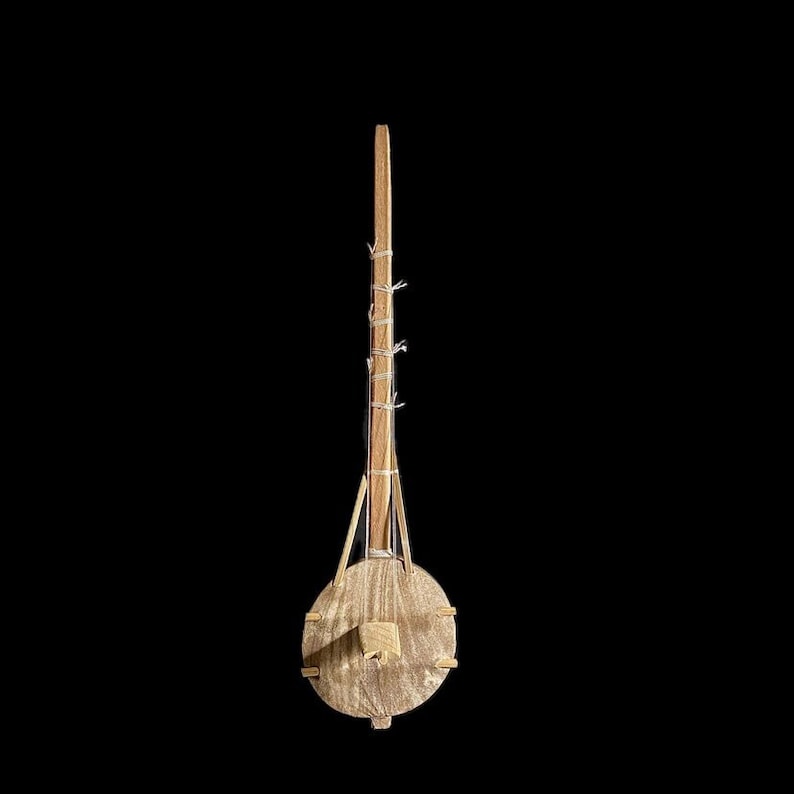 May include: A wooden musical instrument with a round body and a long neck. The neck is wrapped with string and the body has a small wooden piece protruding from the center.