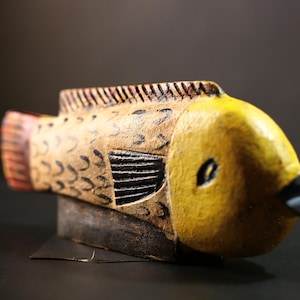 Könnte beinhalten: Eine handbemalte Holzfigur eines Fisches mit gelber, brauner und roter Farbe. Der Fisch hat ein detailliertes Design und eine strukturierte Oberfläche.