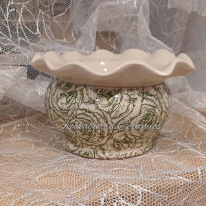 May include: A ceramic bowl with a ruffled rim and a cream-coloured interior. The exterior features a green line-art floral pattern on a cream background. The text Kookaburra Ceramics is printed in a cursive script across the front of the bowl.