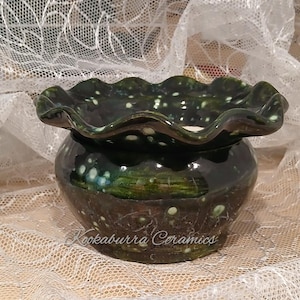 May include: A dark green ceramic bowl with a ruffled, wavy rim and a glossy finish featuring lighter green and white speckled accents. The base of the bowl displays the text Kookaburra Ceramics in a cursive script font across the front surface.