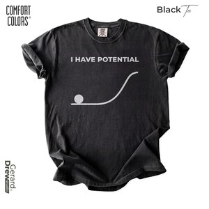 Pode incluir: Uma t-shirt de manga curta cinzento-carvão com o texto branco I HAVE POTENTIAL sobre um gráfico de um círculo numa linha plana que se curva para cima. A t-shirt tem um decote redondo e uma etiqueta de marca visível no interior da gola.