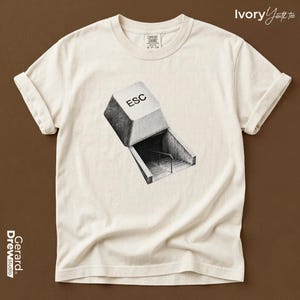 May include: An ivory short-sleeve t-shirt featuring a black and white graphic of a computer keyboard escape key positioned above a concrete staircase leading downward. The shirt has a crew neckline and rolled sleeves, with a label at the neck.