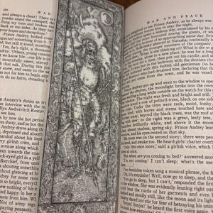 May include: Black and white bookmark featuring a detailed illustration of a warrior figure with a spear, set against a textured background. The bookmark is placed within the pages of a book.