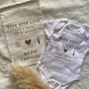 Puede incluir: Una bolsa de lona blanca con el texto "MADE WITH LOVE (and a little bit of science)" y un body blanco con el texto "MADE WITH LOVE (and a little bit of science)". Ambos art&iacute;culos presentan un coraz&oacute;n, un tubo de ensayo y un s&iacute;mbolo de &aacute;tomo.