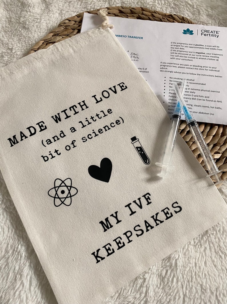 Puede incluir: Una bolsa de lona blanca con el texto "MADE WITH LOVE (and a little bit of science)" y "MY IVF KEEPSAKES". La bolsa tambi&eacute;n presenta un coraz&oacute;n, un s&iacute;mbolo de &aacute;tomo y un tubo de ensayo.