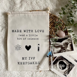 May include: A white canvas bag with the text "MADE WITH LOVE (and a little bit of science)" and a black atom, heart, and test tube symbol. Below the text is "MY IVF KEEPSAKES". The bag is surrounded by ultrasound images and a syringe.