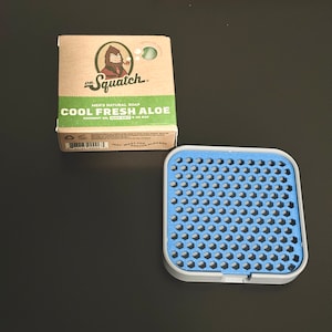 May include: A brown cardboard box with a cartoon image of a sasquatch holding a pipe. The box is labeled "Dr. Squatch" and "Cool Fresh Aloe" with the text "Men's Natural Soap, Coconut Oil, Zero Gritt, 5 oz Bar".