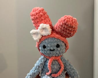 May include: A handmade blue and pink crochet bunny doll. The bunny has large pink ears, a pink scarf, and a white bow. The doll is made of soft, plush yarn and has a smiling face.