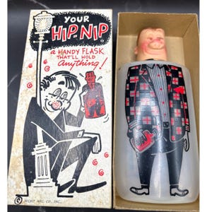 Può includere: Borraccia vintage nella sua scatola originale. La borraccia ha la forma di un uomo con una giacca a quadri e che tiene in mano una borraccia. La scatola recita "Your Hip Nip, a handy flask that'll hold anything!"