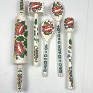 May include: Set of five wooden kitchen utensils with hand-painted floral designs. The set includes a rolling pin, a meat mallet, two spoons, and a small tool. The designs feature red, blue, and green flowers on a white background.