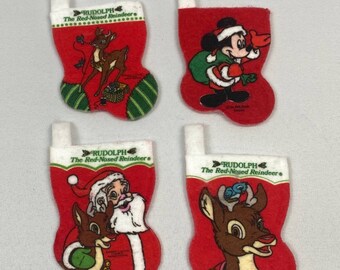 May include: Four small, red Christmas stockings with white tops. Each stocking features a different cartoon character: Rudolph the Red-Nosed Reindeer, Santa Claus, and Mickey Mouse. The stockings have green and white striped accents.