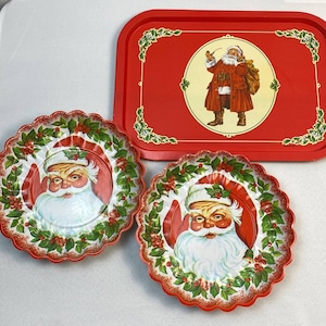 May include: Three vintage Christmas-themed metal serving trays. The largest tray is red with a white border and a picture of Santa Claus in the center. The two smaller trays are red with a white border and a picture of Santa Claus's face in the center.