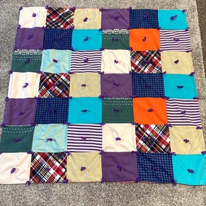 May include: A patchwork quilt with a variety of colors and patterns, including plaid, stripes, and floral designs. The quilt is made of different fabrics and has a rustic, handmade look. The quilt is tied together with purple yarn.