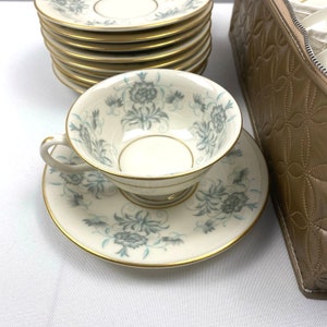 Può includere: Un set di tazze e piattini da tè vintage con un motivo floreale in tonalità di blu e verde. Le tazze e i piattini hanno un bordo dorato e sono in una custodia da trasporto in pelle marrone.