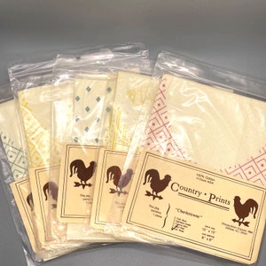 Op de afbeelding: Vijf verschillende kruissteekpatronen met een haanontwerp. Elk patroon is verpakt in een doorzichtige plastic zak met een bruin papieren etiket. De etiketten bevatten de naam "Country Prints", de patroonnaam "Charlestowne", het aantal draden, de maat en de copyrightinformatie.