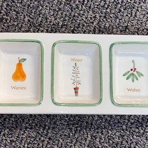 May include: White ceramic serving dish with three sections. Each section has a green border and a festive design. The left section has a pear and the text "Warmest". The middle section has a Christmas tree and the text "Winter". The right section has a mistletoe and the text "Wishes".