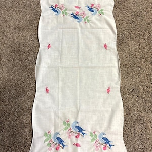 May include: White linen tablecloth with embroidered blue birds and pink flowers. The tablecloth has a scalloped edge.