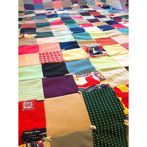 May include: A patchwork quilt constructed from numerous square fabric pieces in a wide variety of colors, textures, and patterns. The squares are joined together with visible white knotted ties at each corner, creating a textured surface.