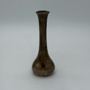 May include: A brown ceramic vase with a slender neck and bulbous base. The vase has a speckled pattern with red accents. The vase is approximately 8 inches tall, making it a decorative piece for any room.