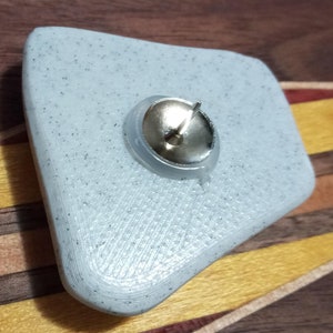 Pu&ograve; includere: Un puntina da disegno in plastica bianca, testurizzata, di forma irregolare con una testa in metallo argentato e una punta affilata.