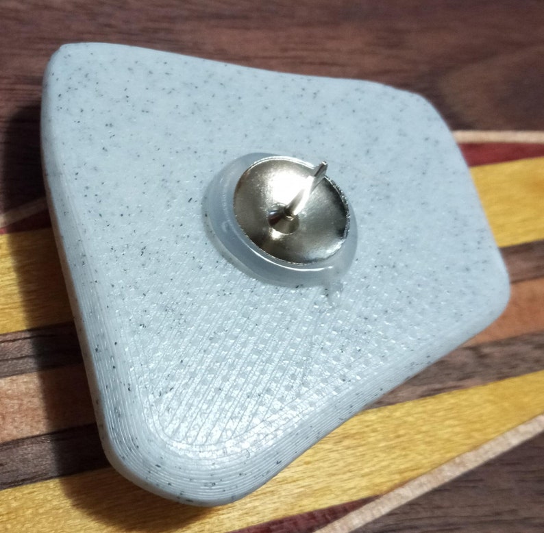 Pu&ograve; includere: Un puntina da disegno in plastica bianca, testurizzata, di forma irregolare con una testa in metallo argentato e una punta affilata.