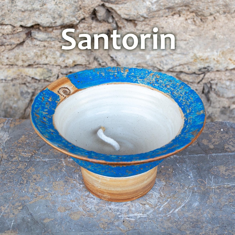 May include: A ceramic bowl with a blue and brown rim and a white interior. The word "Santorin" is written in white across the top. The bowl has a wide, shallow design and sits on a short, cylindrical base.