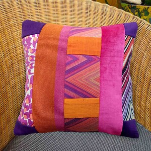 Könnte beinhalten: Ein farbenfrohes Kissen mit Patchwork-Design aus orangefarbenen, rosa und violetten Stoffen. Das Kissen hat ein geometrisches Muster und eine samtige Textur.