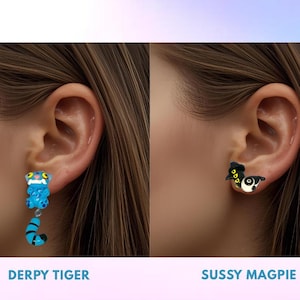 Puede incluir: Pendientes con dos diseños distintos: un "Derpy Tiger" azul y negro y un "Sussy Magpie" negro, blanco y amarillo. Los nombres de cada diseño se muestran debajo de cada pendiente.