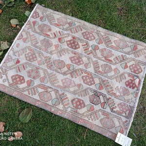 Könnte beinhalten: Ein antiker türkischer Teppich mit einem geometrischen Muster in Rot-, Weiß- und Beigetönen. Der Teppich hat einen abgenutzten und verblassten Look, der ihm einen rustikalen Charme verleiht.