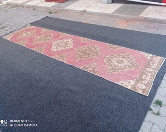 May include: A pink and beige patterned rug with a geometric design. The rug is laid out on a dark gray surface.