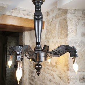 May include: A dark brown wooden chandelier with four arms, each featuring a carved dragon head. The central column has a decorative top and bottom. The chandelier holds four light bulbs. The fixture is suspended from the ceiling.
