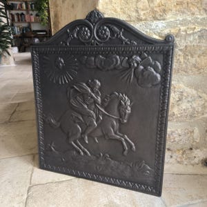 Peut inclure: Un écran de cheminée rectangulaire gris foncé avec un motif en relief orné. L'image centrale représente une personne à cheval, avec des nuages et un éclat de soleil en arrière-plan. Le haut de l'écran présente un motif de volutes décoratives.