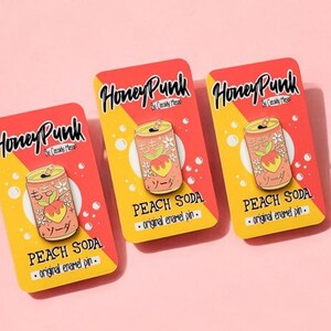 May include: Three peach soda enamel pins on yellow and orange cards with the text "Honey Punk" and "Peach Soda - original enamel pin."