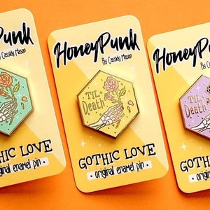 May include: Four enamel pins with a gothic theme. Each pin features a skeletal hand holding a rose with the text "Til Death" above it. The pins are in different colours: green, yellow, pink, and blue. The pins are labelled "Gothic Love - original enamel pin."