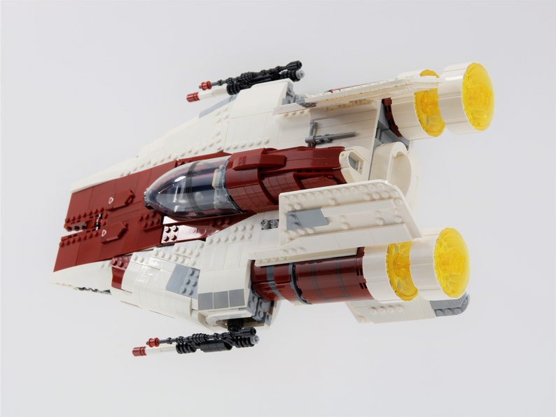 May include: A white and red Lego spaceship with yellow engine exhausts. The spaceship has a clear cockpit and two black guns on the bottom.