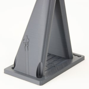 May include: A gray 3D printed stand with a triangular base and two vertical supports. The stand has a small logo on the front.