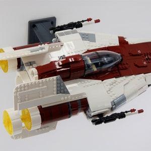 May include: A white and red Lego spaceship with two yellow engines and black guns. The spaceship is suspended in the air.