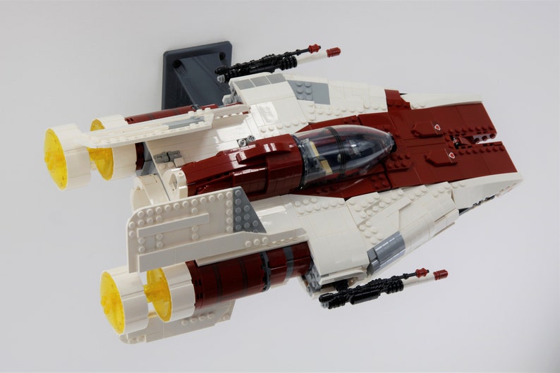 May include: A white and red Lego spaceship with two yellow engines and black guns. The spaceship is suspended in the air.